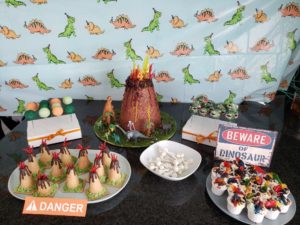 Dinosaur Party Dessert Table with Volcano Cake, Dino Cake Pops, Mini Candy Volcanoes, Dirt Pudding, and Dino Bones